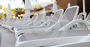 Empty white plastic sun loungers stand in row on beach or by pool on sunny day