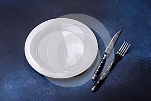 Empty white plate on blue background table. Flat lay
