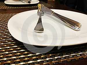 Empty white plate on brown table with knife and fork