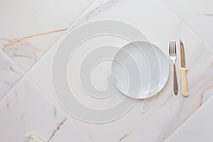 Empty white plate with cutlery on a marble table, saucer, fork and knife. The concept of diet, fasting