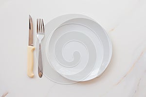 Empty white plate with cutlery on a marble table, saucer, fork and knife. The concept of diet, fasting