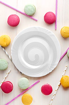 An empty, white plate, with a delicious dessert around, macaroons and tubes for a cocktail. Place for text. Festive