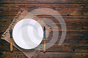 Empty white plate with fork and knife on rustic wooden background