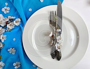 Empty white plate with a fork and knife on a white wooden surface