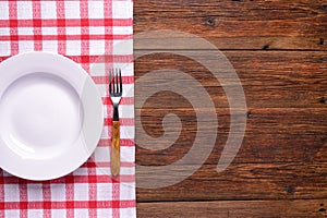 Empty white plate with fork on rustic wooden background