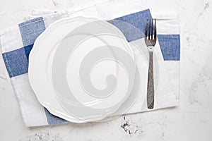 Empty white plate and fork on a table, top view