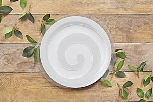 Empty white plate with green leaf on wooden table. Top view.