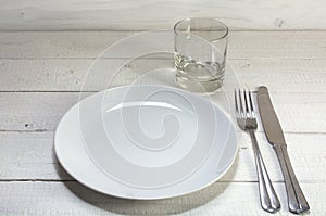Empty white plate with knife, fork and drinking glass on a white