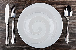 Empty white plate, knife, fork and spoon on table