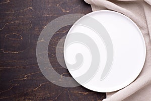 Empty white plate with napkin  on dark wooden table