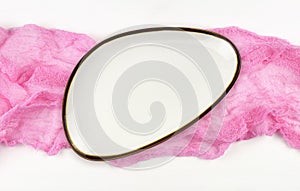 Empty white plate on pink folded cotton textile on white painted wooden table