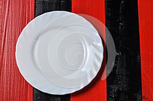 Empty white plate on red and black wooden background