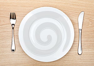 Empty white plate with silverware on wooden table