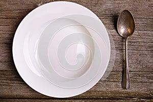 Empty white plate with spoon on rustic wooden background