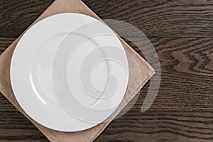 Empty white plate on wood table with napkin