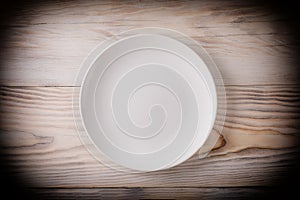 Empty white plate on wooden table with vignette. Top view