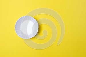 Empty white plate on yellow colored paper background with copy space