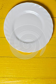 Empty white plate on yellow wooden background