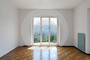 Empty white room with hardwood floors and large windows overlooking the Swiss hills