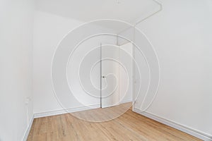 Empty white room with wooden laminate flooring and an open door in new apartment. Concept of preparing the premises for