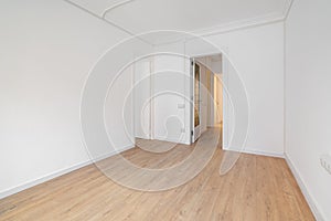 Empty white room with wooden laminate flooring and an open door in new house. Concept of preparing the premises for