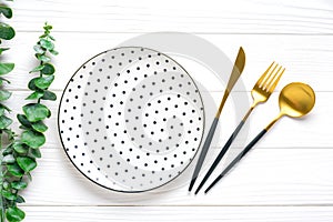 Empty white round plate with black peas, fork, knife, spoon, sprig of eucalyptus on wooden table Top view Flat lay Dishes for