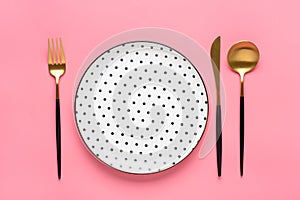 Empty white round plate with black peas, fork, knife, spoon on trendy pink background Top view Flat lay Dishes for breakfast,