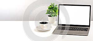 Empty white screen laptop, coffee cup, and vase placed on a white desk in the office. The concept for business, technology,