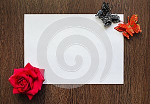 Empty white sheet of paper for your text on a dark wood table background. There are multicolored flowers and butterflies around it