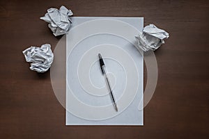 Empty white sheet, pen and crumpled paper on wooden desk