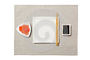 Empty white square plate with chopsticks for sushi, ginger and soy sauce on grey napkin background. Top view with copy space for