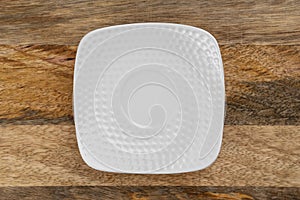 Empty white square saucer on a wooden textured surface