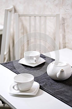 Empty white tea set, cup, saucer and teapot on the table. Porcelain dishes, selective focus