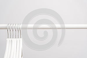 Empty white wooden clothes hangers on a clothing rack against white background