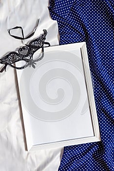 Empty white wooden frame and carnival mask on light and dark textil background