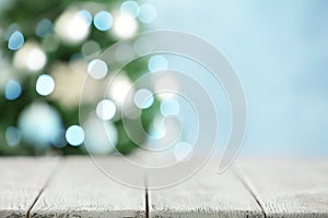 Empty white wooden table and blurred fir tree with Christmas lights on background. Space for design