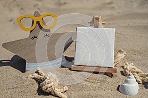 Empty whiteboard frame with copy space for your text or design displays on sandy beach. Starfish in glasses decoration