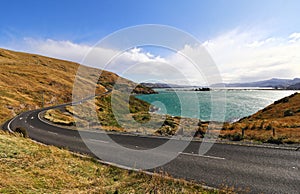 Empty winding asphalt road alongside a body of water in Otago Peninsula, New Zealand.