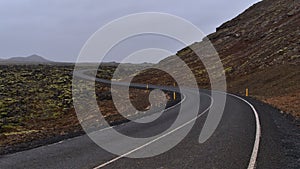 Empty winding country road beside moss covered lava field of volcanic stones near Grindavik, Reykjanes, Iceland.