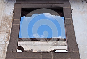 Empty window frame in a roofless abandoned house with white interior walls against a blue sky