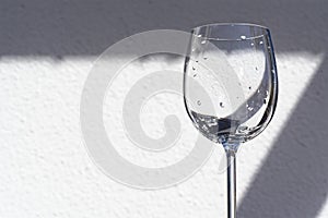 Empty wine glass against white wall on sunny day