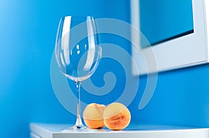 An empty wine glass on a blue background stands on a white table with two peaches