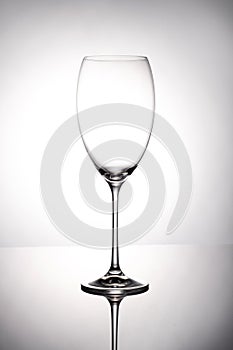 Empty wine glass goblets stands on a mirror surface on white