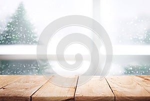 Empty wood table top on blur window view with pine tree in snow