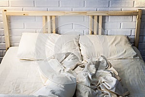 Empty wooden bed in the bedroom, with unmade light duvet