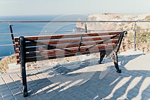 An empty wooden bench with a viewpoint looking out to sea. Wooden bench in city park with sea views on sunny day