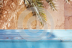 Empty wooden blue table over wall with palm tree shadow background. Summer picnic mock up for design and product display