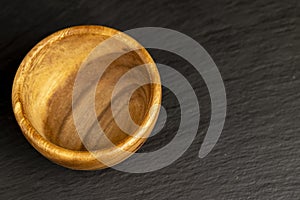 an empty wooden bowl on a black slate table