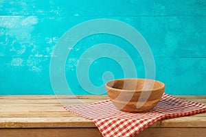 Empty wooden bowl on kitchen table with tablecloth over blue bac