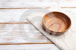 Empty wooden bowl on white wooden background and linen textile. Side view, copy space